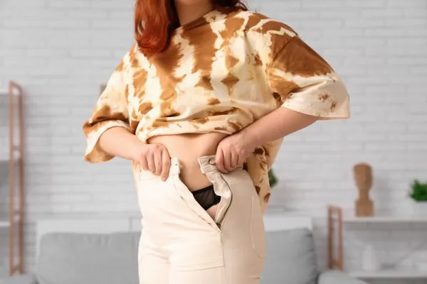Image of woman trying to do her trousers up after pregnancy weight gain Wrexham